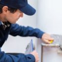 Technician in blue uniform using a measuring device near plumbing tools at City Plumbing service location.