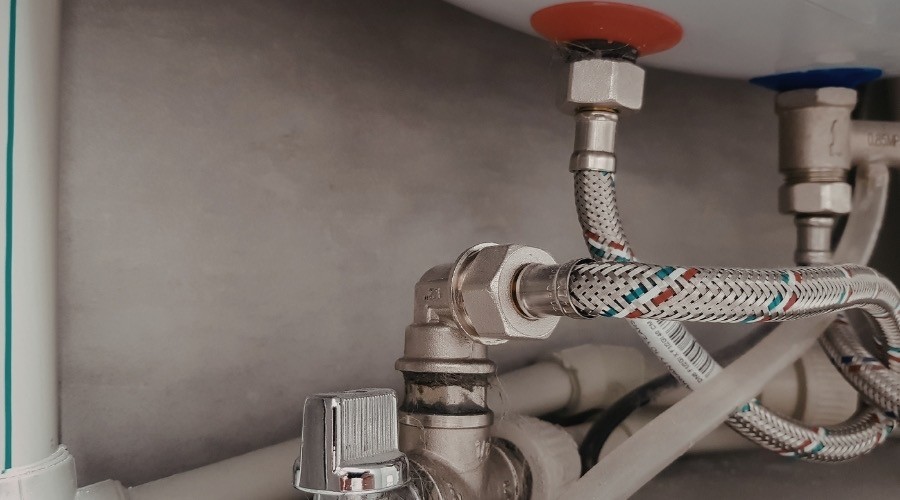 Plumbing pipes and valves under sink, illustrating plumbing services and maintenance.